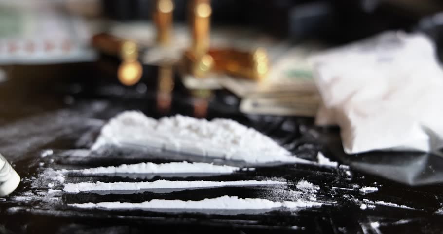 Snorting a line of cocaine with a rolled dollar bill on black background, slow motion. Illegal drugs and cash with gun and bullets on table - crime scene. Criminal problems. Illegal selling