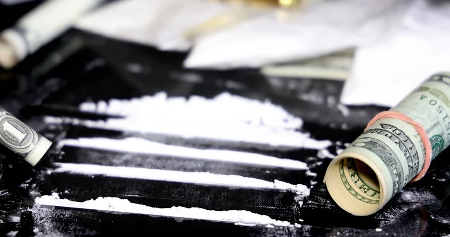 Snorting a line of cocaine with a rolled dollar bill on black background, slow motion. Illegal drugs and cash with gun and bullets on table - crime scene. Criminal problems. Illegal selling