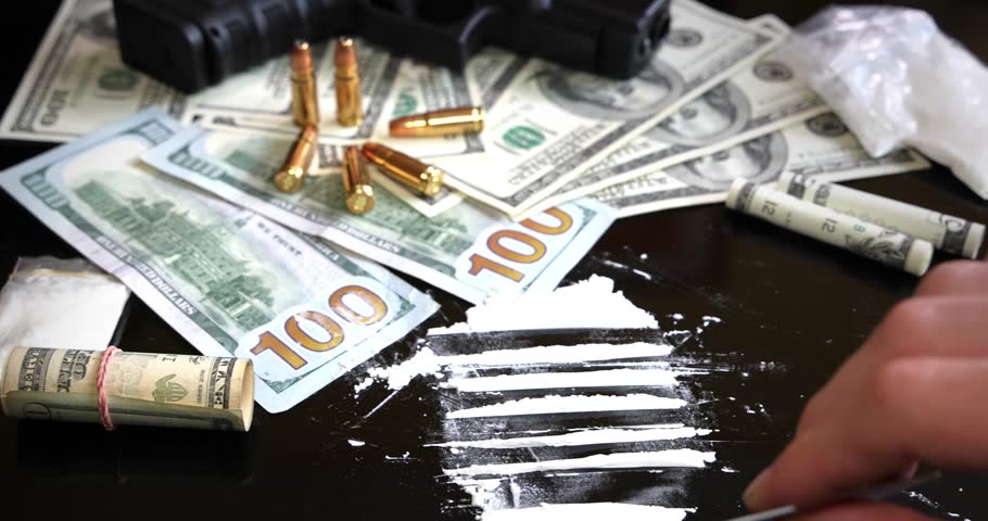Illegal drugs and cash with gun and bullets on table - crime scene. Man making cocaine line with credit card. Criminal problems. Drugs and money on black background. Illegal selling
