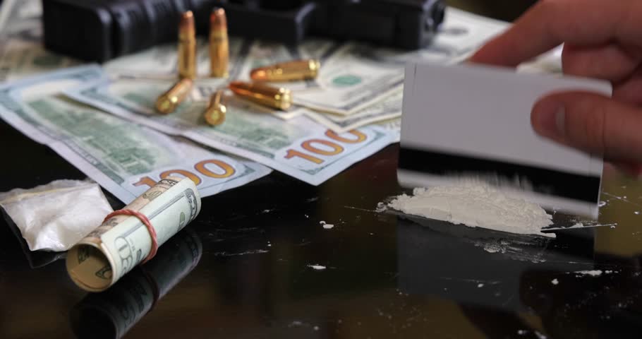 Illegal drugs and cash with gun and bullets on table - crime scene. Man making cocaine line with credit card. Criminal problems. Drugs and money on black background. Illegal selling