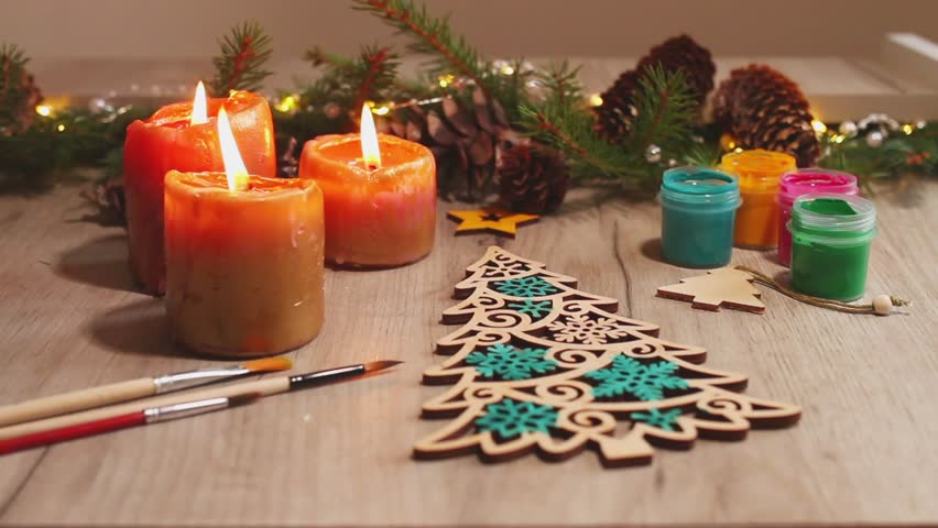 Winter painted wooden toy Christmas tree with brushes, paints, spruce branches, pinecones and candles on table