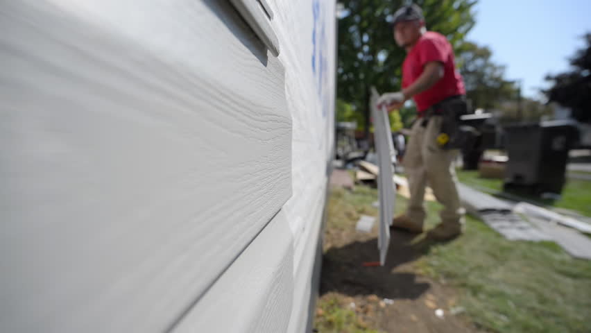 A worker installing plastic panel siding on the outside wall of the residential house