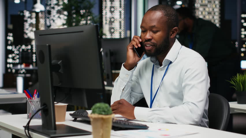 African american business analyst making a phone call late at night to ensure upcoming schedule, discussing with his partner on telephone line. Busy manager showing professionalism. Camera B.