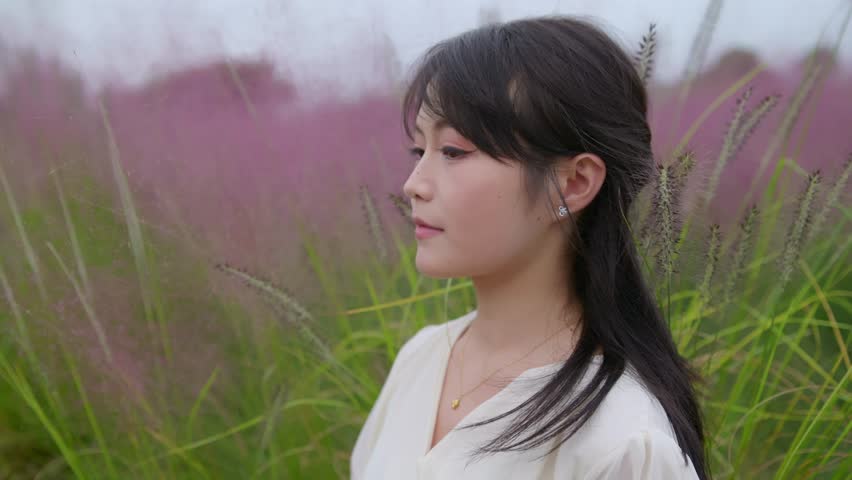 A beautiful Asian girl sits among pink muhly grass, looking up at the sky.