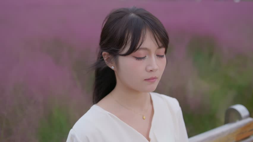 A beautiful Asian girl sits among the pink muhly grass, closing her eyes and quietly feeling the breath of nature.