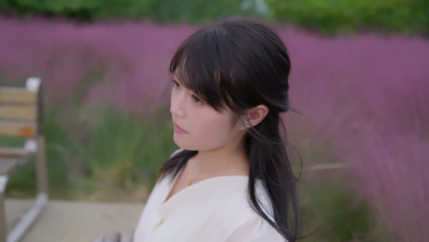 A beautiful Asian girl wearing a white long dress is among the pink muhly grass.