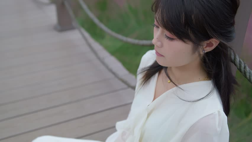 A beautiful Asian girl wearing a white long dress is sitting next to pink muhly grass, looking very relaxed and enjoying the surroundings.