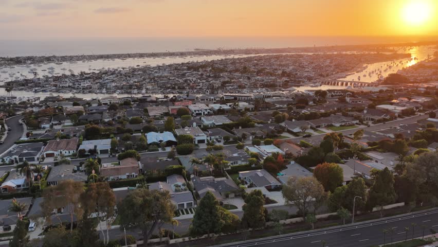 Drone shot of coastal Orange County, California at sunset with the Newport Beach harbor in view.