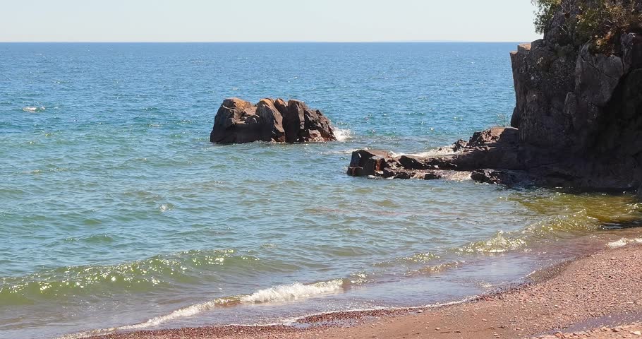 A beach, waves and trees at the rocky North Shore of Lake Superior in northern Minnesota on a sunny day.
