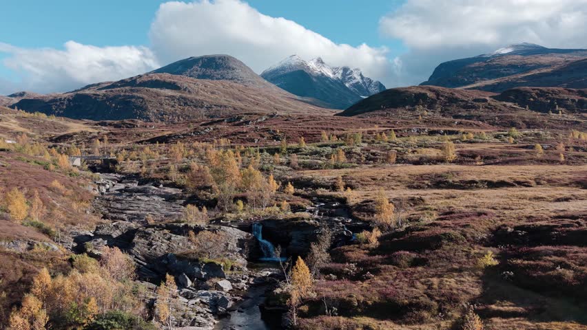 A drone video capturing autumn colors in Jotunheimen National Park, with a stream flowing through the autumn colored mountain valley