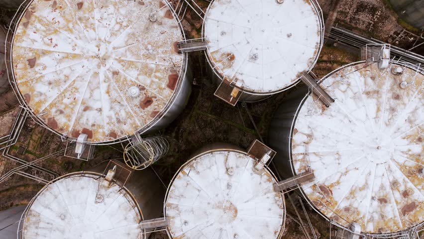 Aerial cinematic vertical drone footage over oil tanks, symbol of old energy era