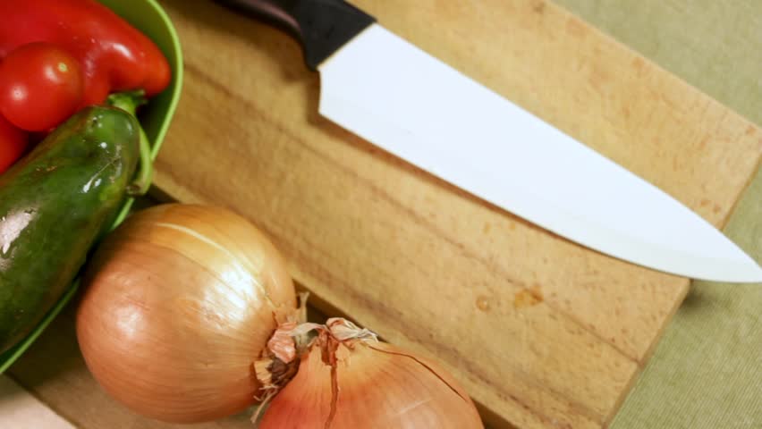 Male hands hold fresh bell pepper on wooden board with onion, tomatoes and knife. Bell pepper shows vivid color and texture, pepper near vegetables highlights beauty. Concept of healthy homemade food.