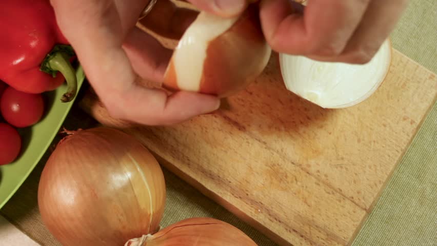 Male hands peel onion on wooden cutting board, showing natural cooking in cozy kitchen. Male hands hold onion with vegetables nearby, stressing wholesome preparation. Concept of healthy homemade food