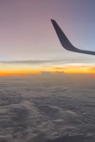 Airplane wing above clouds during vibrant sunset.