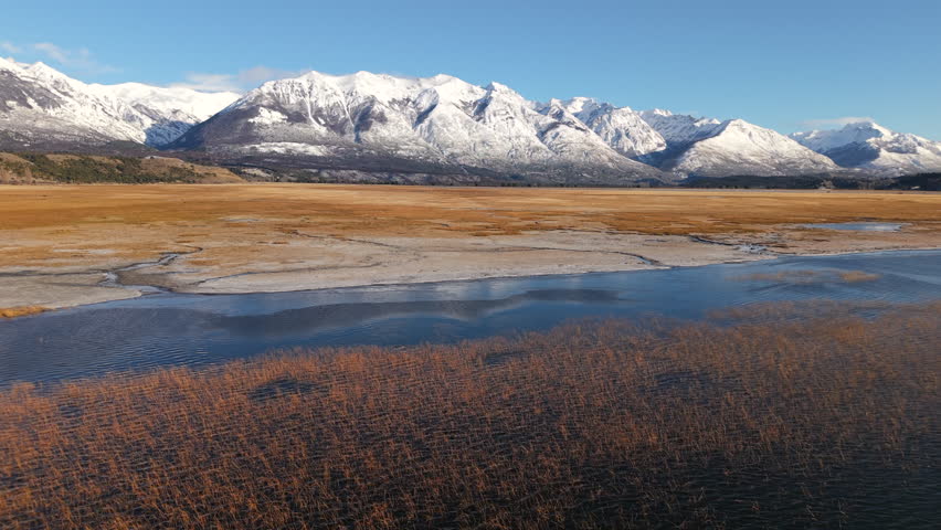 Flat golden terrain, and snow-covered Andean peaks in the background, blending geography, ecology, and visual storytelling from Chubut Province, Patagoniam a lake stretches across the steppe