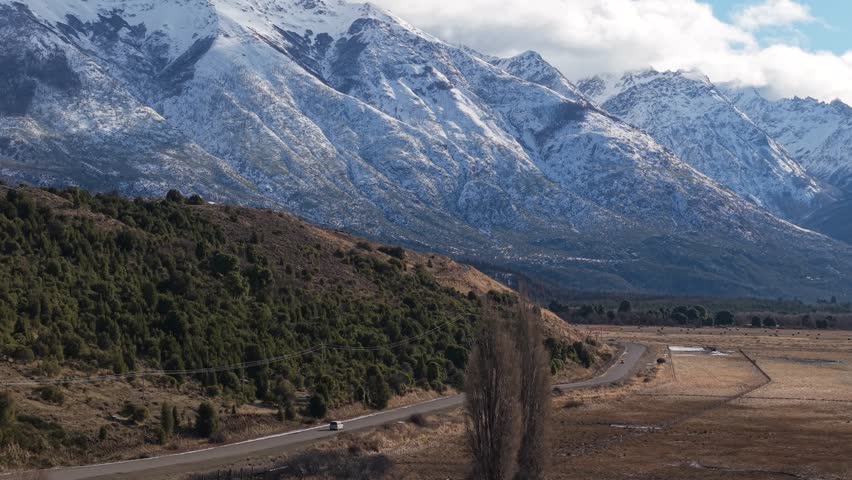 Drone glides over Ruta Provincial 71, revealing winding road through dry valleys and snow-capped Andes framed by native lenga trees, steppe grasses, and rugged beauty of Los Alerces Establishing Shot