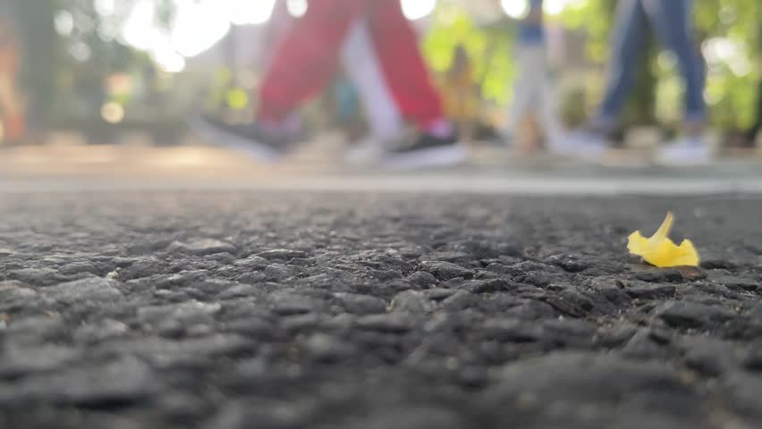 Low angle asphalt macro with yellow leaf in focus. people walking in soft bokeh. Natural morning light, clean negative space. ideal background for fitness promos, urban reels, text overlays, openers.