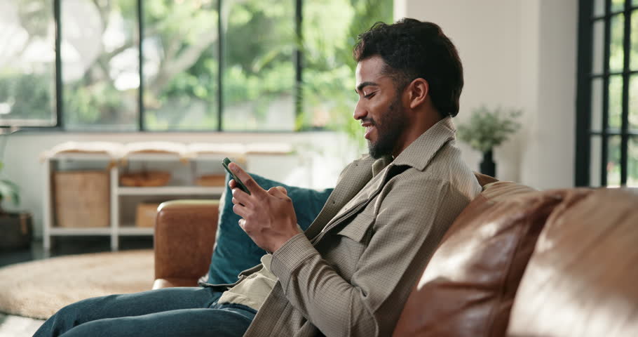 Laughing, phone and typing with man on sofa in living room of home for relax or social media browsing. App, break and funny with person in apartment for me time, mobile communication or text message