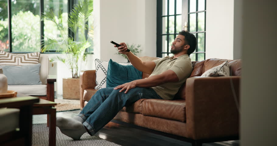 Watching tv, relax or man on sofa with remote, series or sports broadcast on weekend break. Chill, movie binge and male person in house with tech, multimedia streaming and subscription on Sunday rest