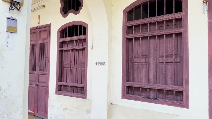 Camera slowly pans across vintage wooden doors and windows, bright daylight, old town Phuket architecture