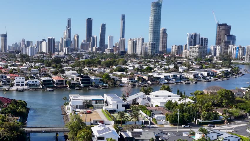 Drone pans across canal homes and high-rise skyline under bright daylight, Gold Coast, Australia
