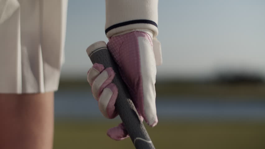 Woman golfer adjusts grip on golf club standing on country course