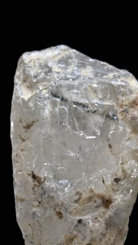 Colourless Quartz with needle-like Schorl Tourmaline crystal inclusions, rotating slowly against a black background. Vertical.