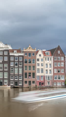 Hyperlapse of colorful Canal Houses on Damrak in evening light, reflected in water with boats passing by under dramatic clouds timelapse. A charming view of Amsterdam, Netherlands