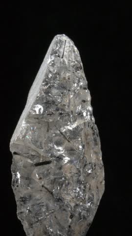 Colourless Quartz with needle-like Schorl Tourmaline crystal inclusions, rotating slowly against a black background. Vertical.