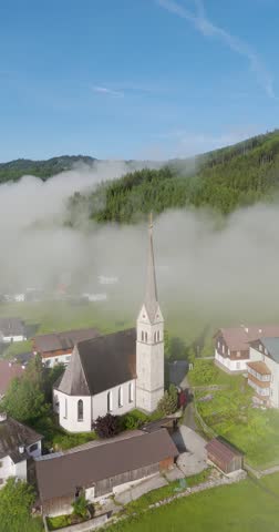 "Pfarrkirche" "Gosau" in Austria old gothic church peaking through the clouds in a valley