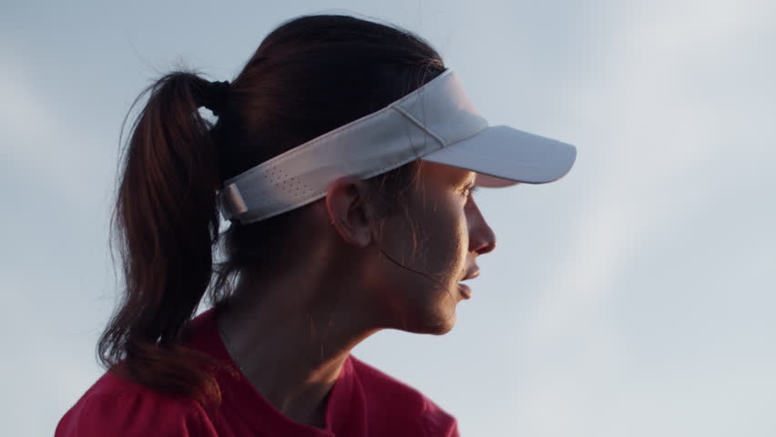 Woman stands with golf club looking at golf ball preparing swing