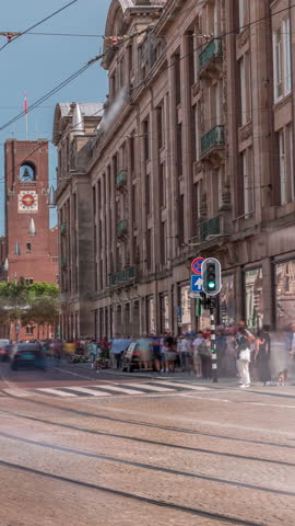 Electric tram on Damrak Street heading from Dam Square to Centraal Station in a timelapse. Traffic moves on the road while people wait at the tram stop. Amsterdam, Netherlands
