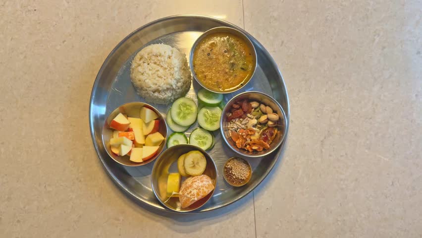 Top-down view of a healthy Indian thali served with rice, dal, fruits, nuts, and seeds in a stainless steel plate, symbolizing a balanced vegetarian diet and Indian home-style meal.