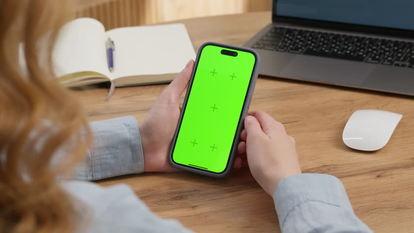 Woman sit use digital tech cell phone, green screen mock up. Hand scroll iphone web site, swipe like photos. Girl hold mobile closeup. Chroma key page. Cozy office background. Online app copy space.
