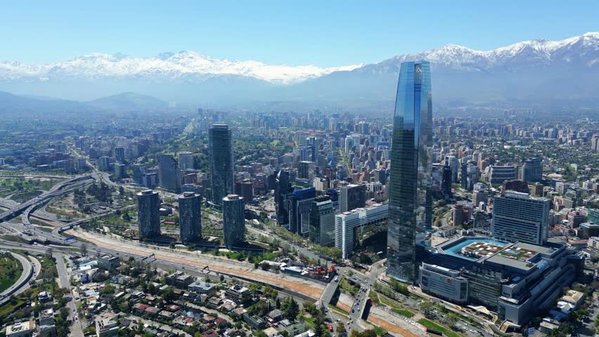 Santiago, Chile drone aerial panning over downtown skyline and Costanera Tower with snowcapped Andes in clear daytime.