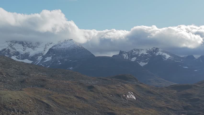 Backwards flying drone footage showing clouds over mountains and autumn colored hills in Jotunheimen National Park