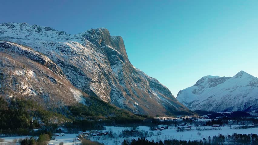 aerial view captures the serene winter beauty of Eresfjorden in Norway. Snow capped mountains rise dramatically above a tranquil fjord, with scattered houses nestled in the valley below.