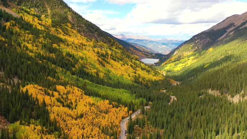 Silverton, Colorado bursts with color as cars wind through bright aspen groves and narrow mountain switchbacks framed by rugged peaks and clear blue sky.