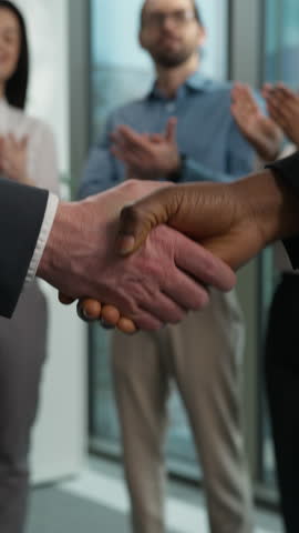 Two businesspeople shaking hands handshake agreement deal contract client director success diversity happy workers in background applaud congratulations celebrate office business company partnership