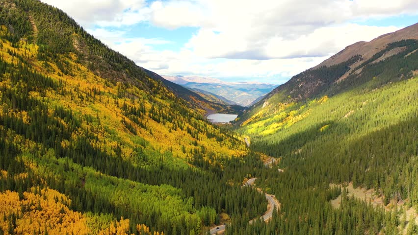 The Canadian Rockies stretch across the horizon as brilliant aspens fill the valley and peaks reflect in alpine lakes under crisp blue autumn light.