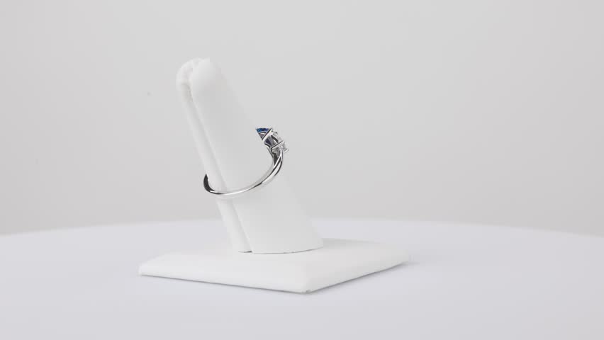 Elegant sapphire ring spinning slowly on a jewelry stand against a clean white background.