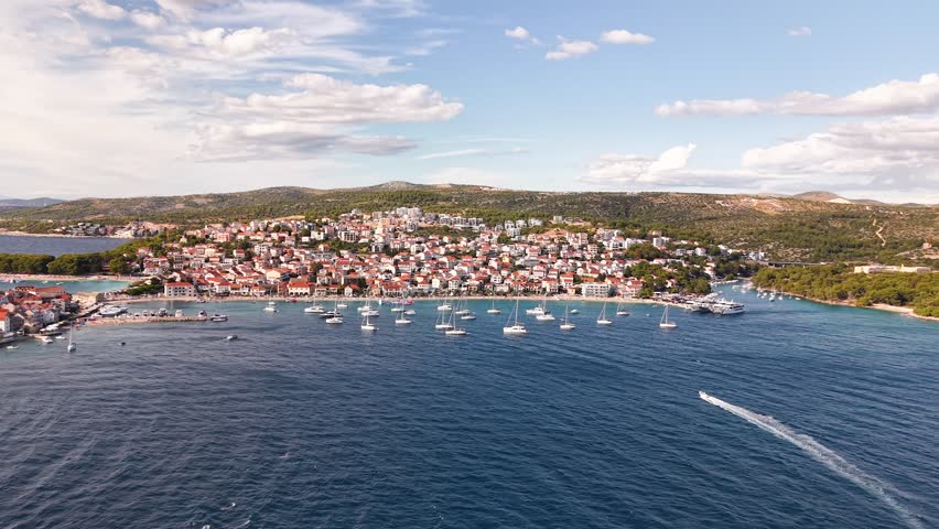 Breathtaking landscape of a beautiful Croatian town along the azure Adriatic Sea, featuring a bay filled with sailboats and a scenic backdrop of green mountains, inviting tranquility and adventure