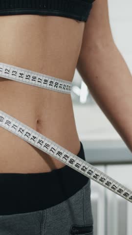 A woman is measuring her waist with a measuring tape for fitness tracking. Weight loss, health and body measurements to monitor progress and goals.
