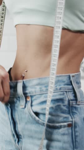 A person uses a measuring tape to check their waist size while wearing loose jeans. Weight loss concept