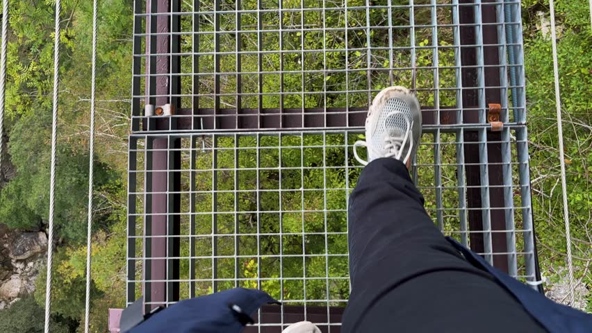 First-person view on a metal grate suspension bridge over Okatse Canyon. Breathtaking views of lush green forest below. Thrilling, adventurous journey high above nature.