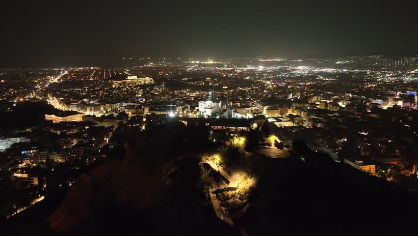 Aerial drone cinematic night video of iconic Lycabettus hill with chapel of Saint George with great views of illuminated city of Athens, Attica, Greece