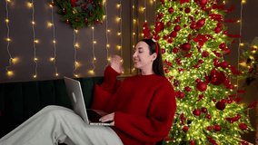 Woman in red sweater and reindeer headband makes a video call on laptop in front of a glowing Christmas tree, sharing festive greetings and holiday joy perfect for seasonal and digital themes - Powered by Shutterstock - Get 15% off with code: PIKWIZARD15