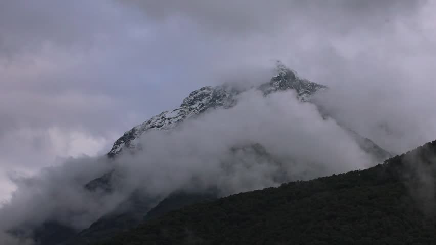 Serene landscape featuring rolling green hills under a cloudy sky. Mountains are partially obscured by mist, creating a tranquil atmosphere.