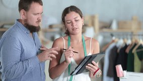 Friendly young female fashion designer developing clothing design on tablet while discussing and refining details with engaged male client in sewing studio - Powered by Shutterstock - Get 15% off with code: PIKWIZARD15