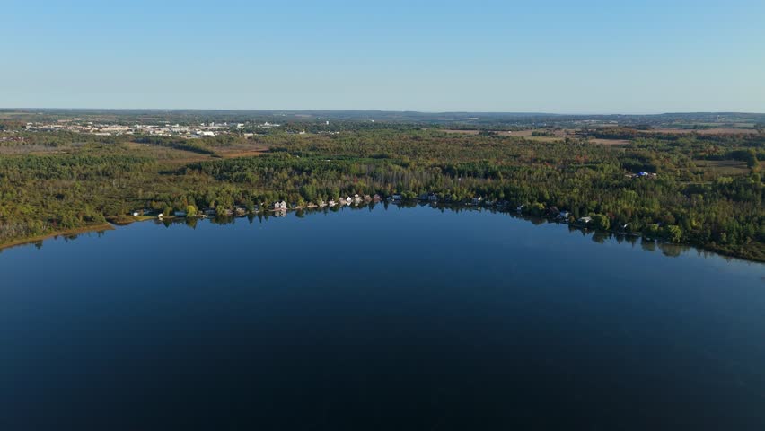 A stunning aerial view of waterfront cottages lining the shore of the private Caledon Lake in Ontario. The vast autumn forest and the town of Orangeville are in the background.